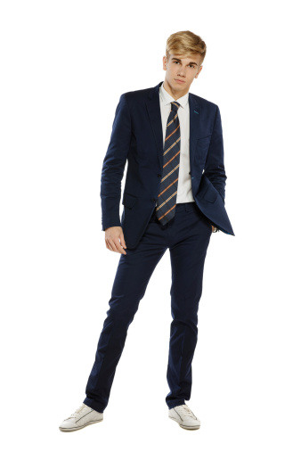 Full length portrait of a stylish young man in suit standing with hand in pocket over white background