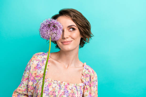 Photo of minded adorable lady fresh flower cover one eye look empty space imagine isolated on teal color background stock photo