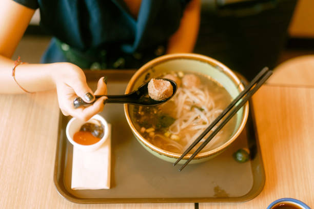 Close Up Asian Woman Eating Large Pho Noodle in Restaurant Alone with Vietnamese Coffee stock photo