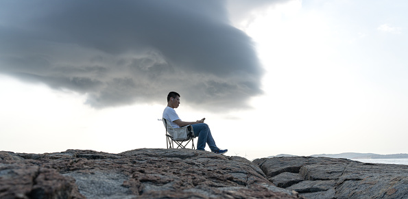 Young men sit on rocks when black clouds cover the top