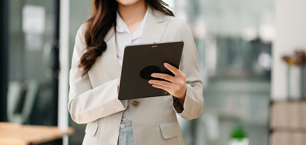 Confident Asian woman with a smile standing holding notepad and tablet at the modern office.