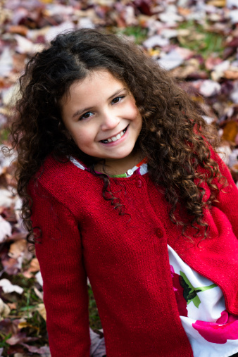 Young Hispanic girl sits in the park on Autumn day against a background of leaves.