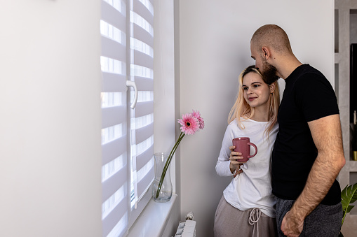 A beautiful young couple in love exchange affections by the window in the living room