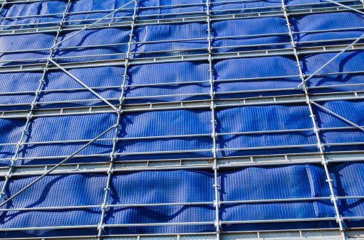 Metal scaffolding at construction building site with the blue cover-up, is made from steel tubes that are set jointly by steel fittings