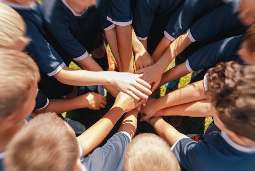 Many Happy Children Stacking Their Hands In A Teamwork Effort Before Playing Sports Game. Junior Football Team Stacking Hands Before a Match