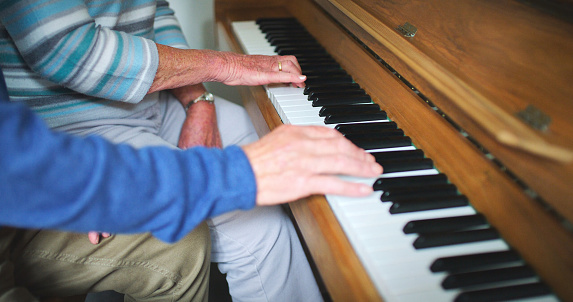 Hands, music and playing the piano together at home for performance, hobby or to relax in a room. A senior man and woman on a vintage instrument with keys, notes and keyboard at a house in retirement