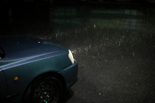 Car in rain. Lamp of car shines through raindrops. Trip at night in storm. Bad weather on road.