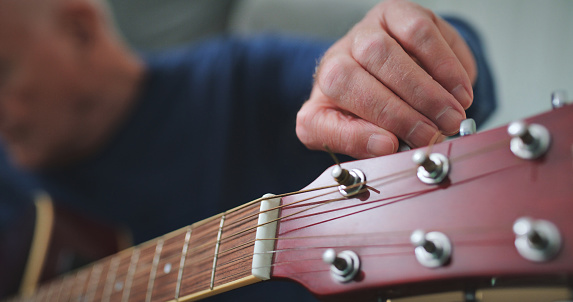 Man, tuning guitar and hands in home living room to play song for music in house. Person, acoustic instrument and musician check notes in lounge for sound, audio and creative closeup for performance