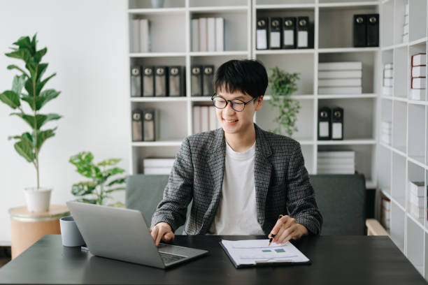 istock Young business man working at modern office with laptop, tablet and taking notes on the paper. 1566891478