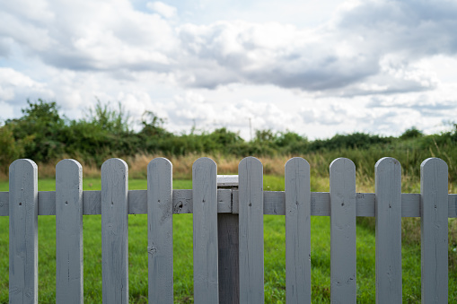 Newly painted wooden picket fence seen bordering a private garden with a nearby wild meadow on the edge of a housing estate in the UK.