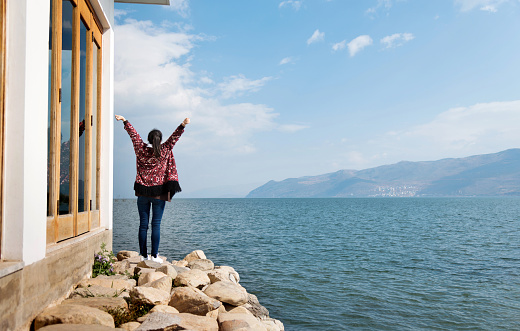 Woman standing by the lakeside with arms raised.