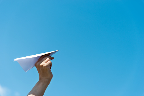 Woman hand holding a paper plane under blue sky.