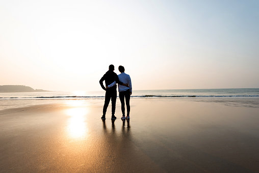 Romantic couple standing on beach at sunset.