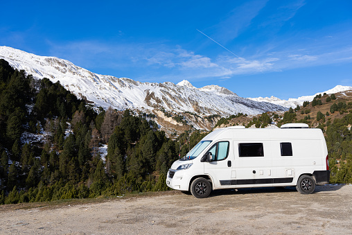 6m long white camper van in the mountains. The Camper is parked in an unpaved square and you can see the left side. The VanLife in the mountains in Switzerland.