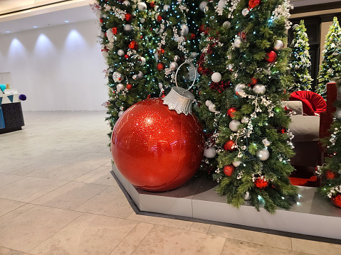 A super large red ornament by a decorated wall for Christmas.