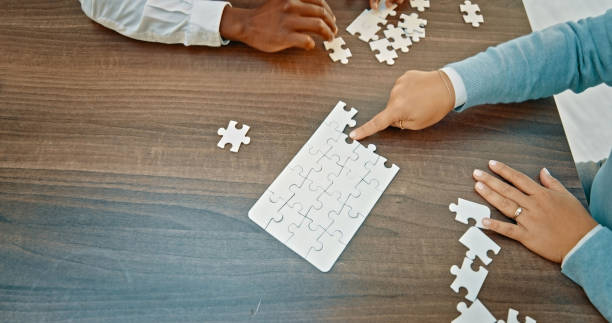 istock People, hands and pointing to puzzle above for team building or problem solving activity at office. Top view of group in teamwork for partnership, brainstorming or jigsaw solution on table or mockup 1566956348