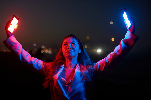 woman posing holding up red and blue neon lights at night outdoors at night