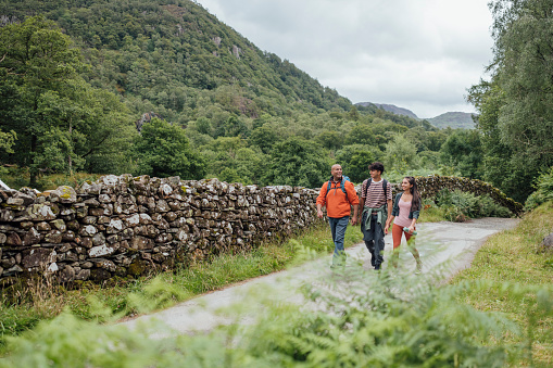 A wide angle front view of a father and his two teenage children who are out enjoying a hike together in Keswick in the Lake District in cumbria. They are carrying rucksacks with supplies as they take on a scenic trail.