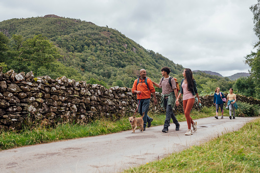 A wide angle view of a family of five enjoying the beauty of the Lake District in Keswick in Cumbria. They are out walking their patter-dale terrier along a beautiful quiet country road.