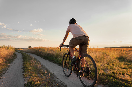 Cyclist riding on a trail in field on gravel bike at sunset. Travel and active lifestyle concept.
