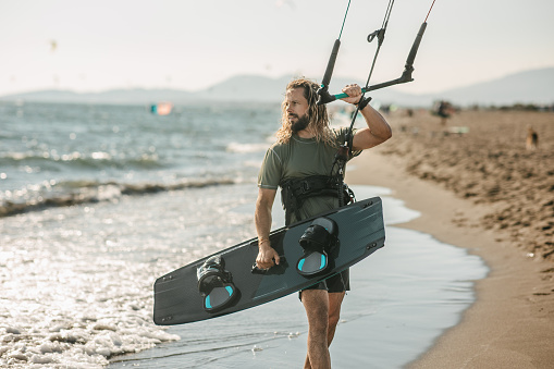 Portrait of a kite surfer standing by the sea water after a ride on a kiteboard in Montenegro, Ada Bojana, and holding kite board. Wild look, long hair, and tanned skin.