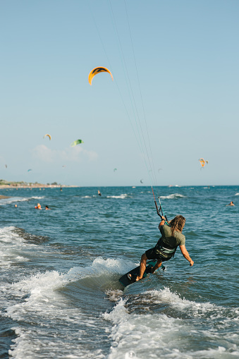 Sports kitesurfer in the air doing a trick with a wakeboard, rider in a wetsuit on a clear blue sky in a parachute jump, looking at the camera. Water sports.