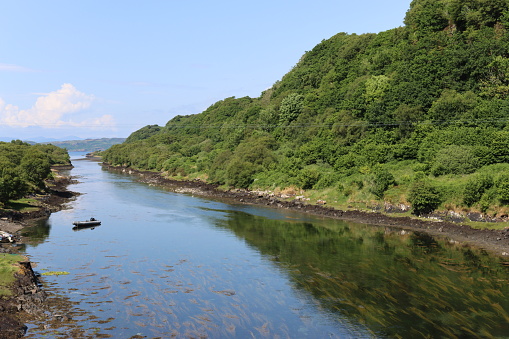 View along a wide river with green woodland reflected in still water