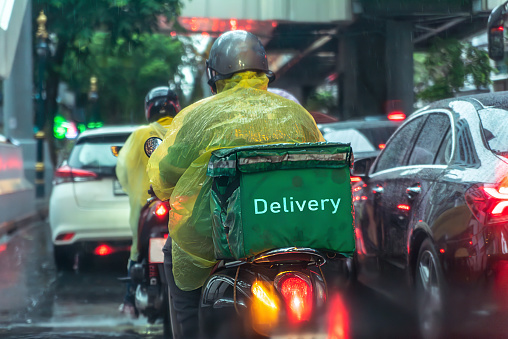 food delivery via motorcycle Traffic bottleneck was cleared by a courier wearing a helmet and a disposable plastic raincoat.  food delivery on bike. service that delivers food