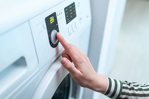 Housewife using display and button for turning on and choosing cycle program on washing machine for laundry at home