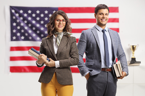 Young man and woman holding books in front of a USA flag