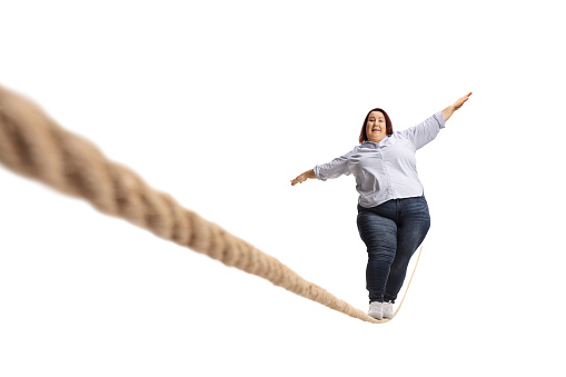 Full length portrait of a scared overweight woman walking on a rope isolated on white background