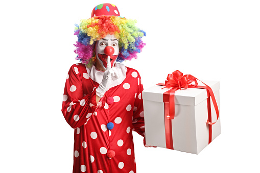Clown with a birthday present making a finger mouth shush sign isolated on white background