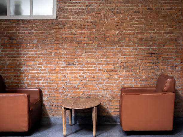 istock Brown luxury modern leather single sofa, side view with round wooden side table decorated on empty brick wall background. Loft style interior design with furniture and brick construction. 1567078231