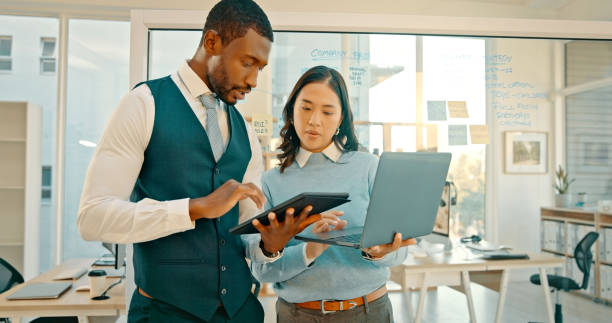 istock Tablet, laptop and people in business talking about project or communication, conversation and employees working together in office. Teamwork, technology and woman coaching businessman about strategy 1567080489