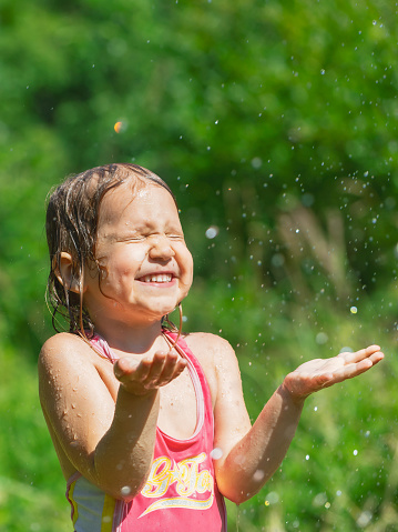 Happy little girl enjoying playing with a garden sprinkler on a hot summer day