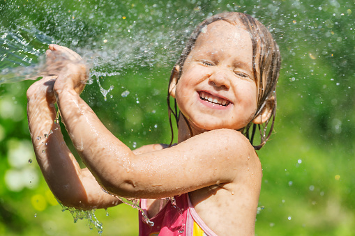 Happy little girl wearing swimsuit enjoying playing with a garden hose jet on a hot summer day