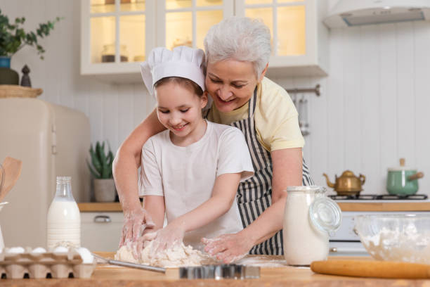 счастливая семья на кухне. бабушка и внучка вместе готовят на кухне. бабушка учит девочку замешивать тесто, печь печенье. семейная командна� - grandmother domestic life cooking domestic kitchen стоковые фото и изображения