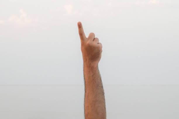 istock Hand doing, showing number one gesture symbol on bright blue summer sky nature background. Gesturing number 1. Number one in sign language. First and counting one concepts. 1 finger up 1567112410