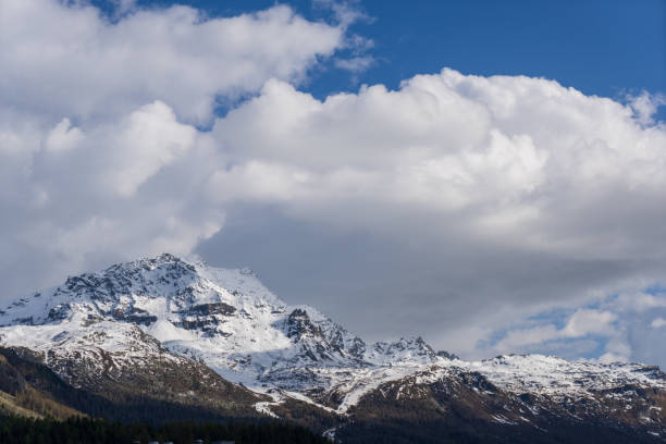 Snow-capped mountains under blue skies and white clouds in summer. St. Moritz Retreat: Capturing the Scenic Landscapes of a Swiss Vacation Town.