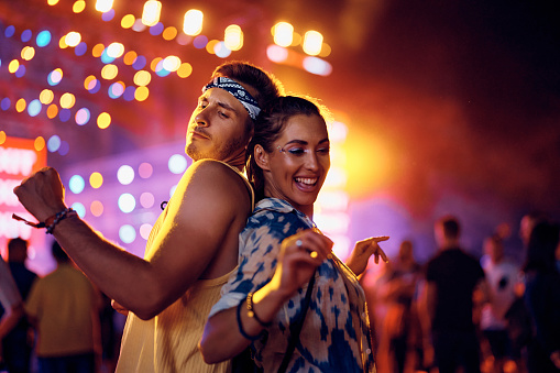 Young cheerful couple of festival goers dancing in front of music stage at night.