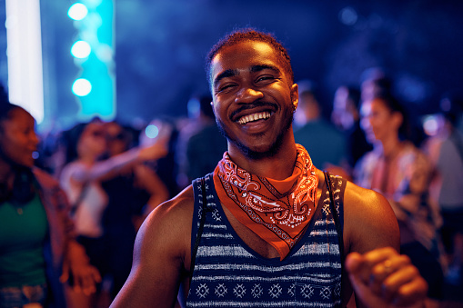 Cheerful African American man having fun and dancing while attending summer music festival at night and looking at camera.