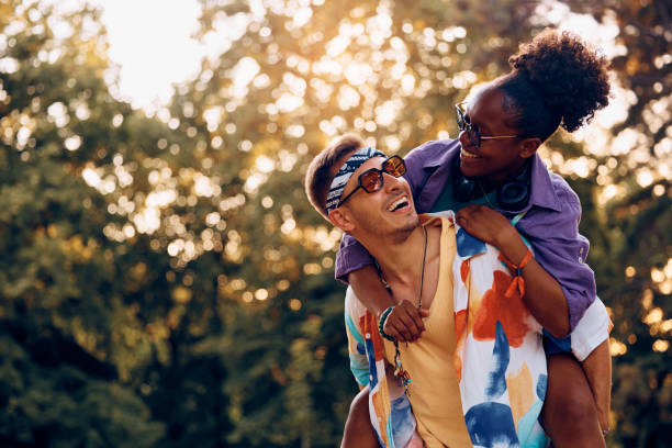 Cheerful couple having fun while piggybacking in the park on summer day.