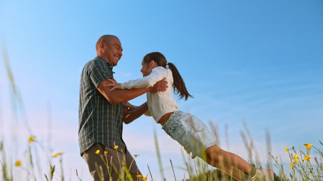 SLO MO Father spinning his daughter in the sunny meadow
