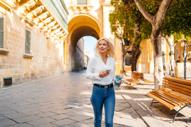 istock Young Woman Using Phone While Drinking Coffee And Walking In Valletta Malta 1567132738