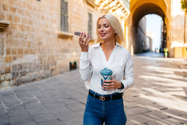 young woman sending a voice message while drinking coffee and walking in valletta malta - vocoder imagens e fotografias de stock