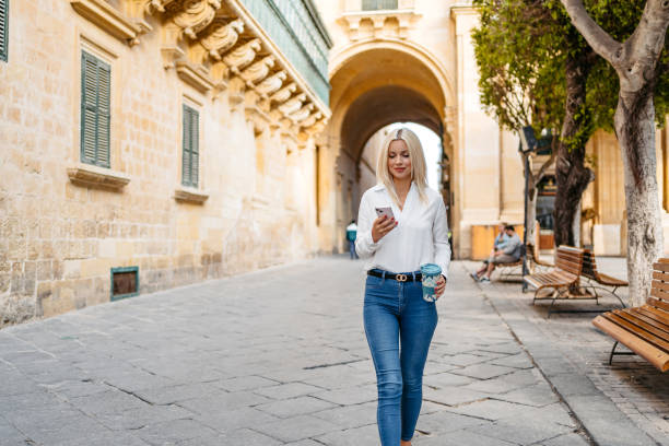 istock Young Woman Using Phone While Drinking Coffee And Walking In Valletta Malta 1567140389