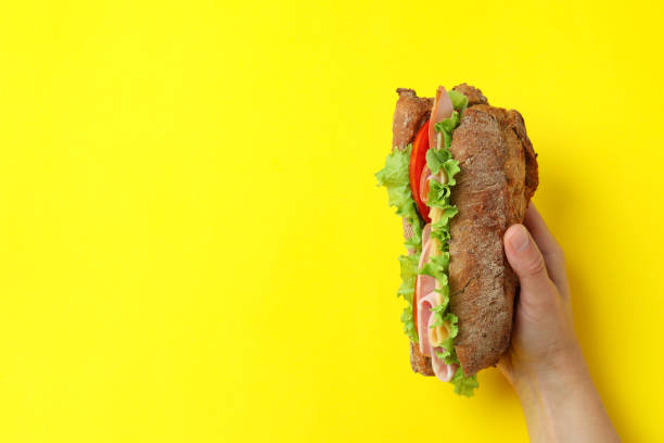 istock Female hand holds ciabatta sandwich on yellow background 1567141966