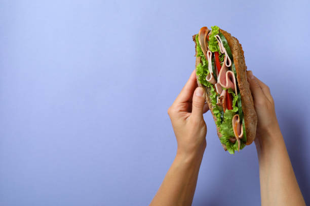 istock Female hands hold ciabatta sandwich on violet background 1567146292