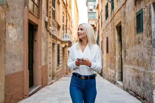 Beautiful young blonde woman texting on her smart phone in an alley in Valletta, Malta.