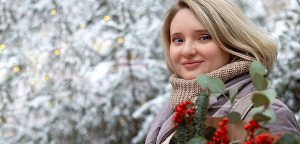 Portrait of young woman holding Christmas bouquet on snowy background. Copy space.